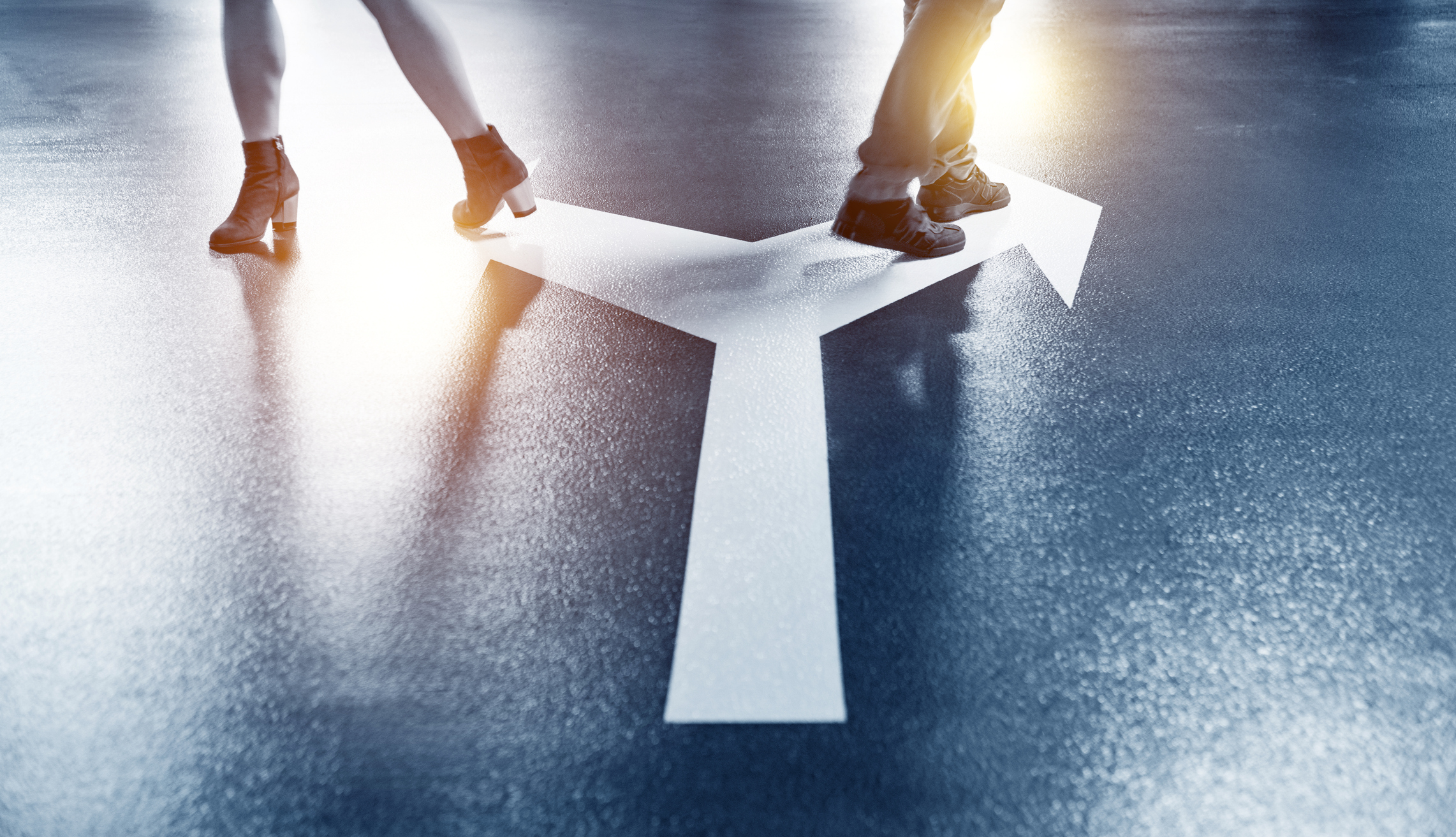 Legs of two people on a road with a split road sign on the road