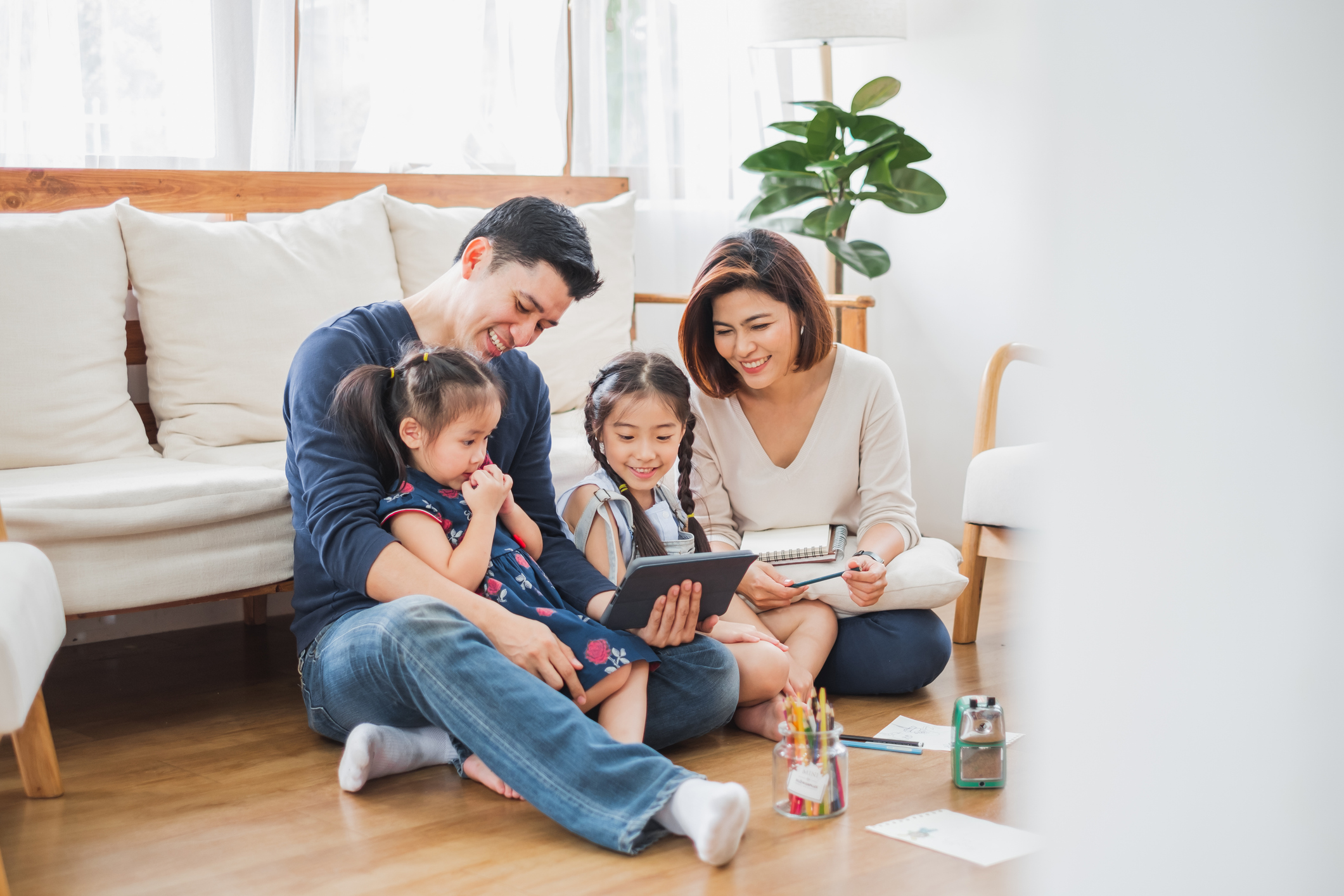 Father, mother and two daughters sitting on the floor and watching an iPad with smile