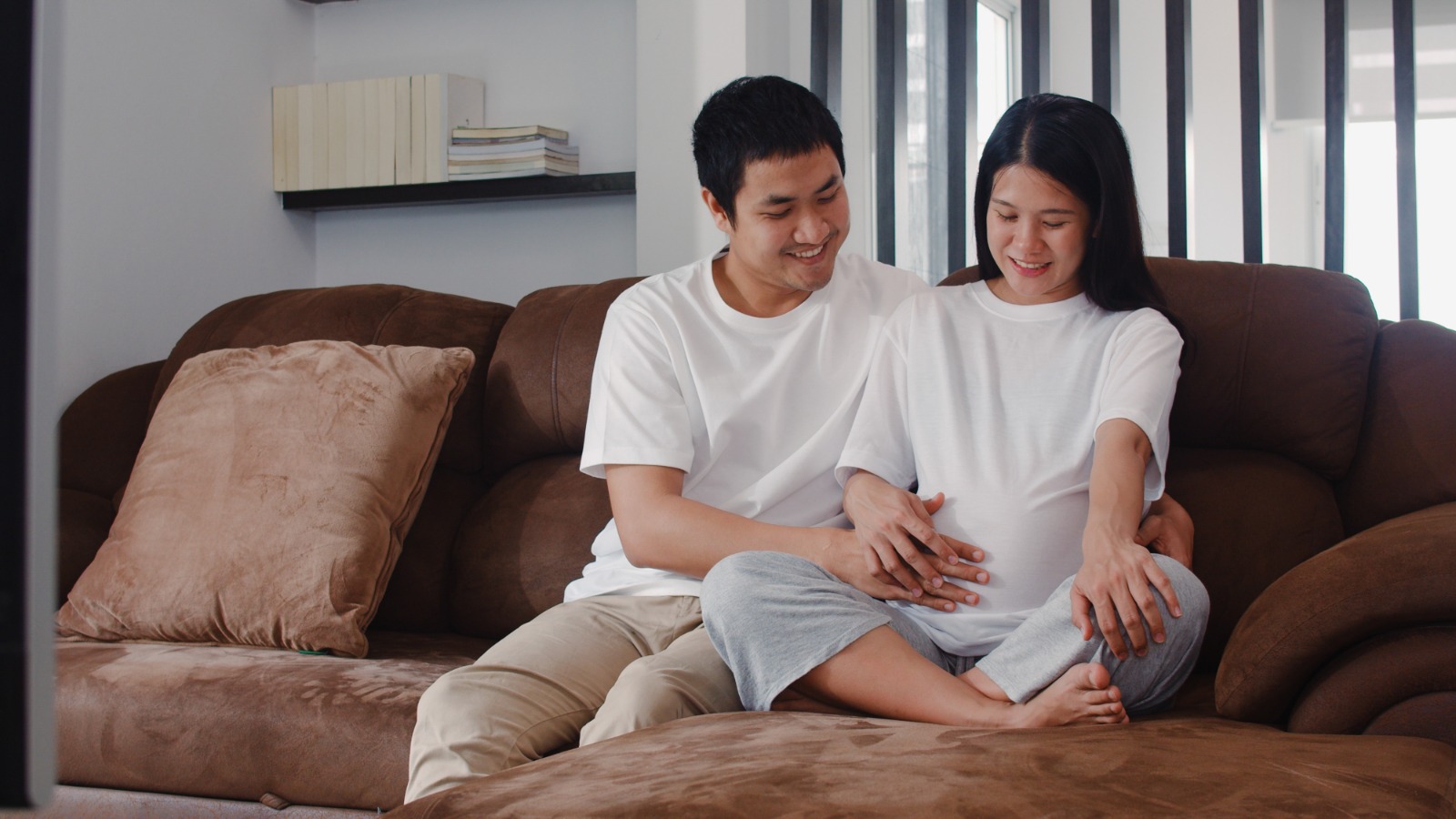 Man aand woman sitting on a cotch and holding hands on the woman’s belly