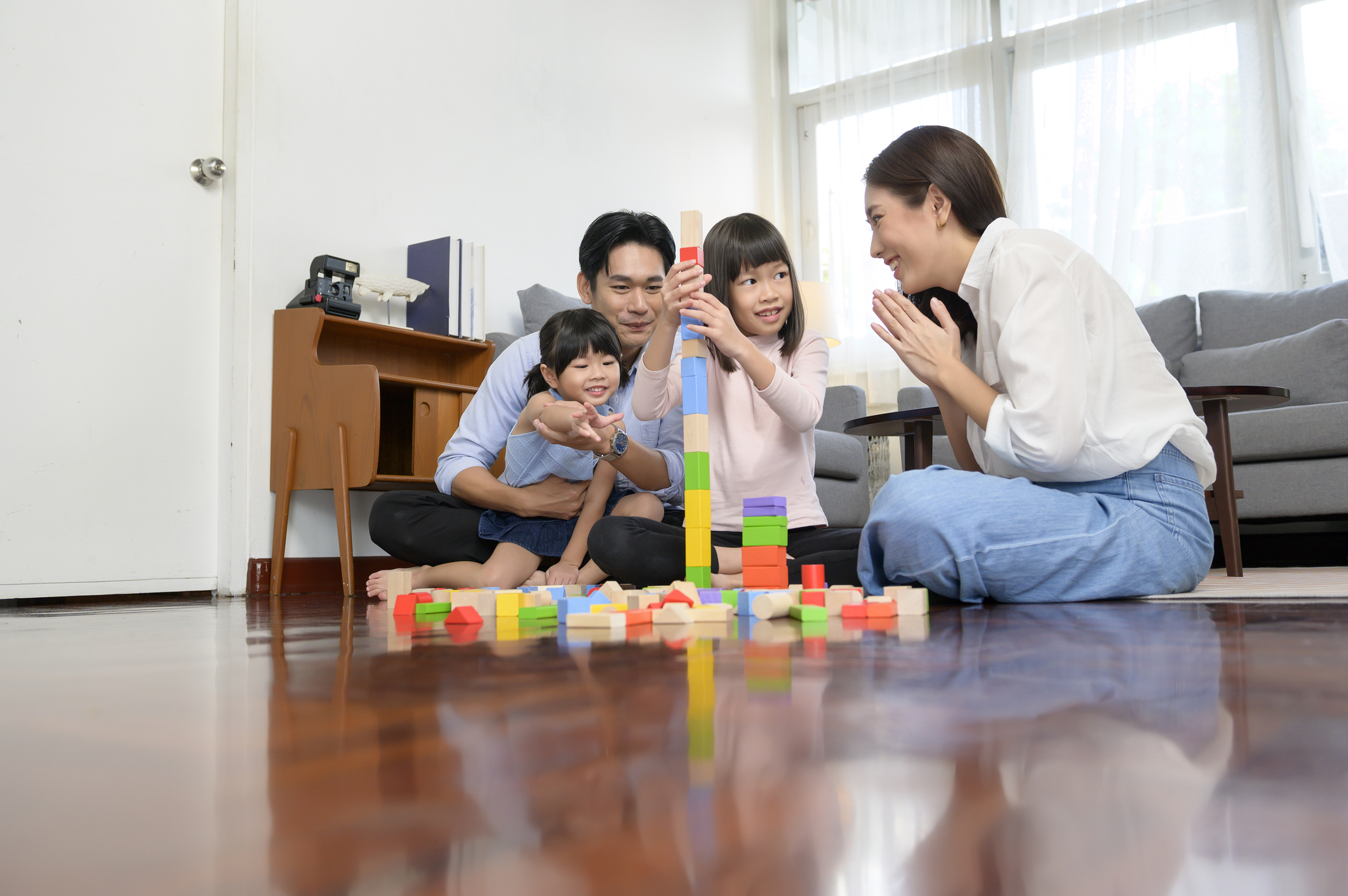 Asian family with children playing and building tower of colorful wooden toy blocks in living room at home