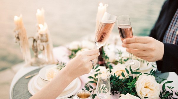 Man and woman holding champagne and toasting on a wedding-decorated table