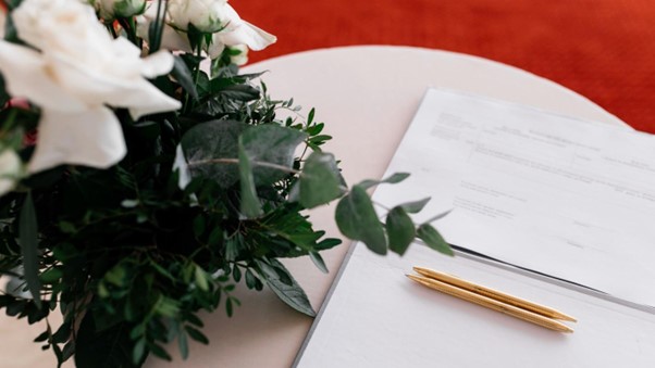 A stack of documents with two pens on a table next to a plant