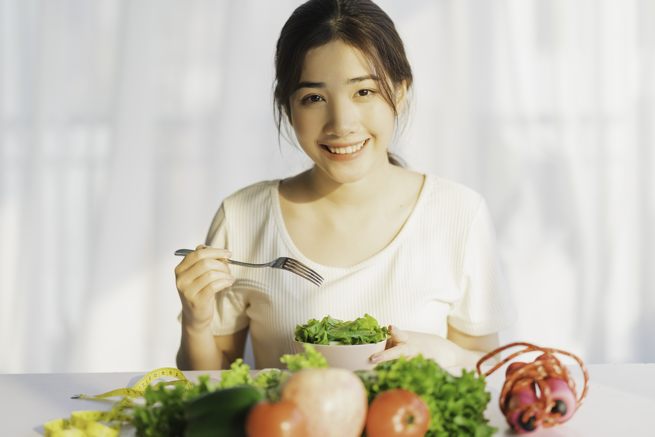 Young woman eating a bowl of vegetables and smiling at you