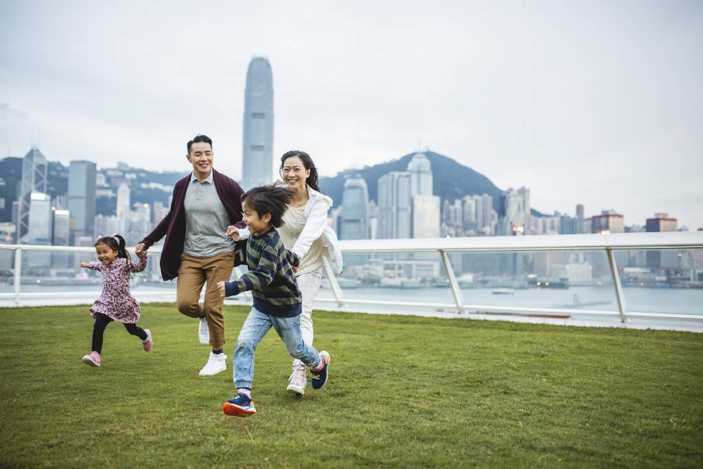 Mother and father holding hands and running with two children on a grass field