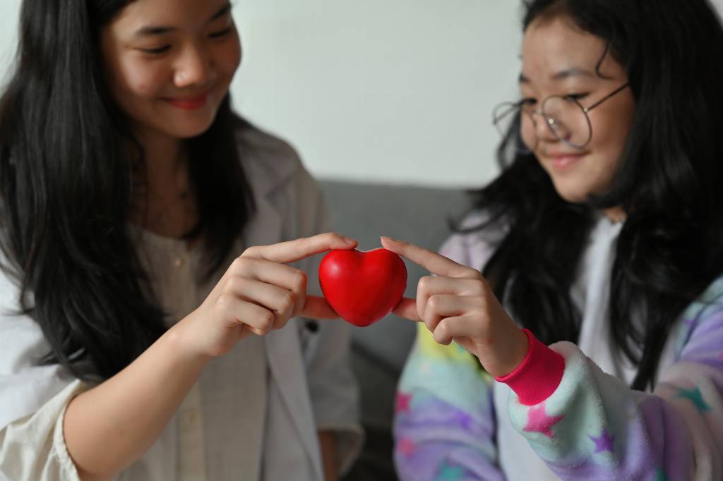 Two young girls holding a heart together with a smile.