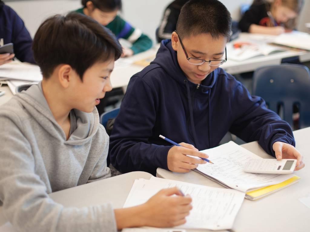 Two students holding a calculator and writing on a notebook.