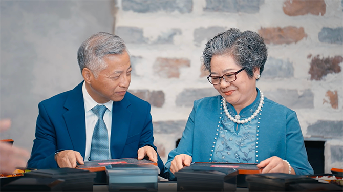 Old man and woman sitting on a table and holding a stack of paper