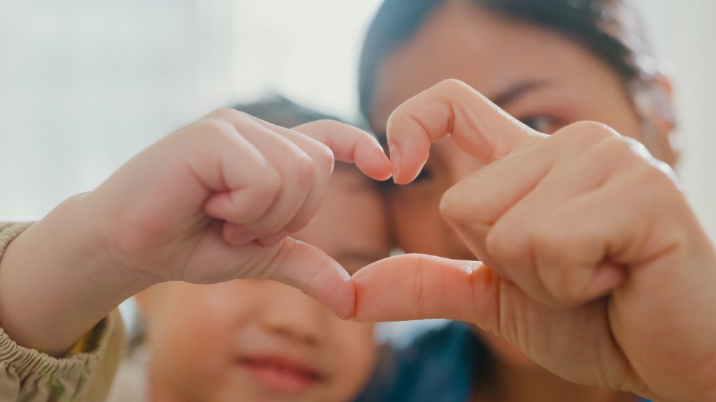 Closeup of mother and child making fingers heart shaped signs at home