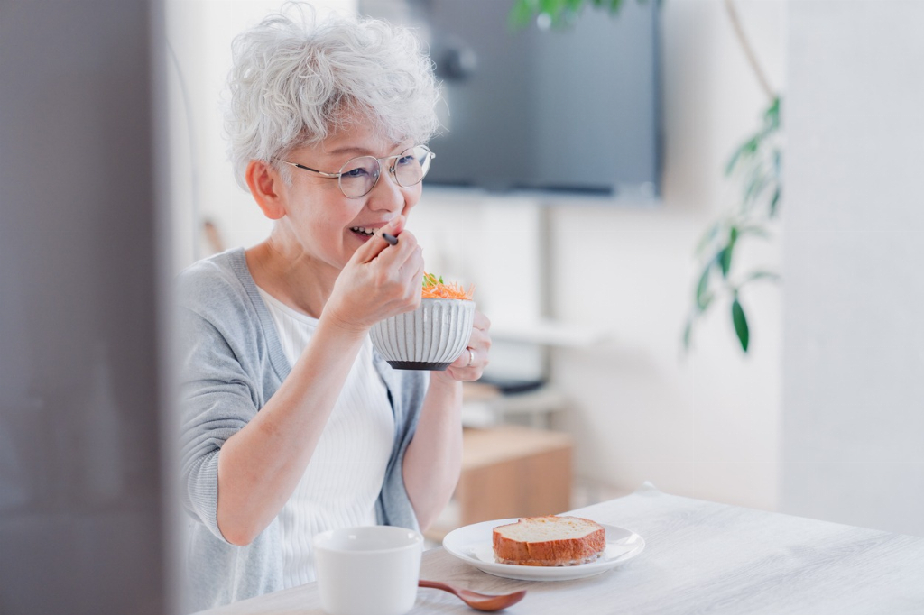 Elderly woman eating healthy salad while relaxing in her living room